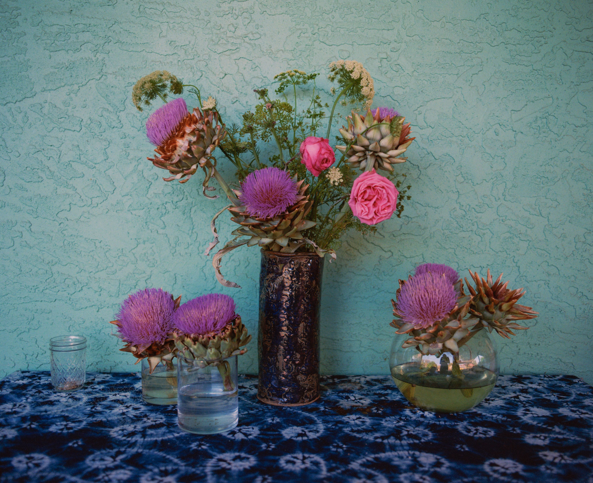 Violetfarbene Blumen und Artischocken in Vasen draußen im Garten auf einem Tisch.